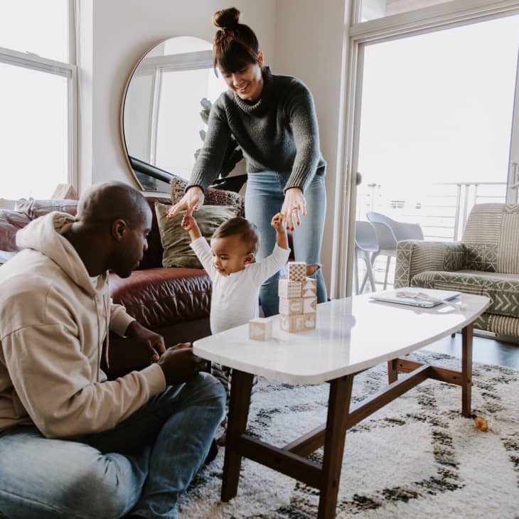 Family playing with wooden blocks in a cozy living room with a round mirror and patterned rug.