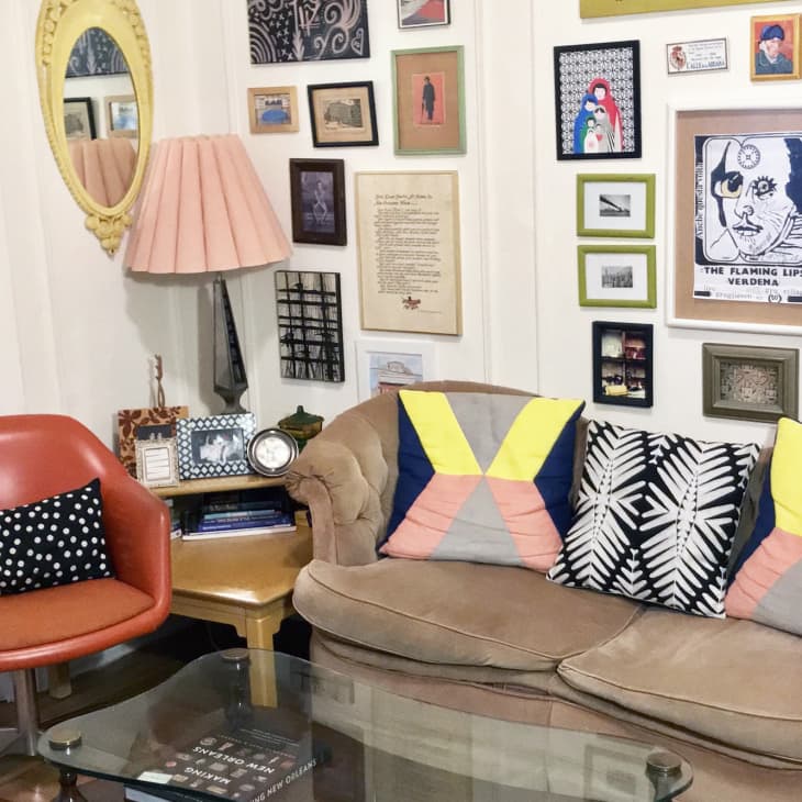 Eclectic living room with a tan sofa, colorful pillows, orange chair, and a gallery wall of framed art and photos.