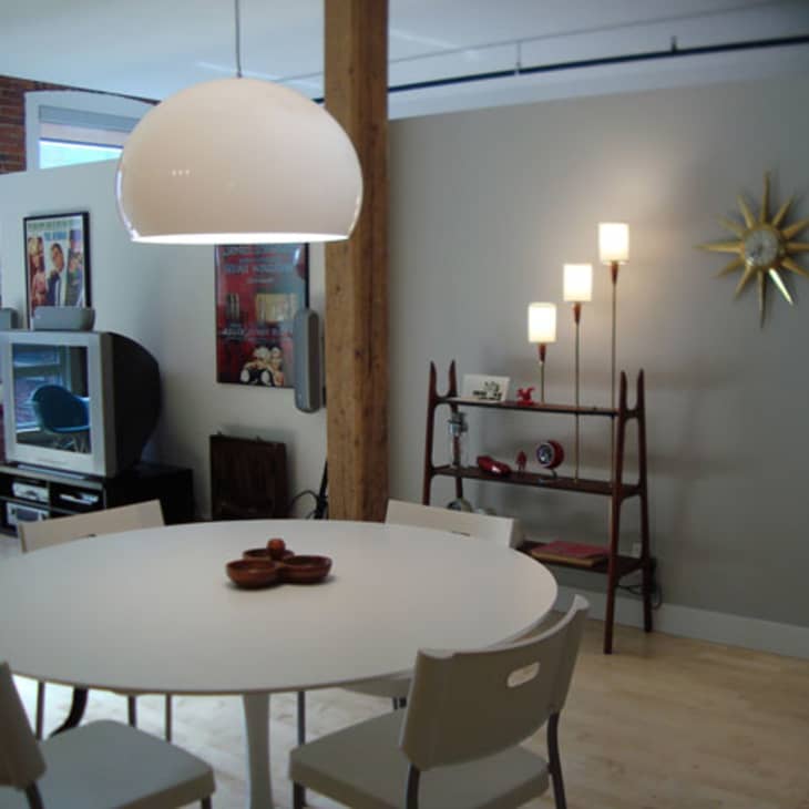 Modern dining area with round white table, four chairs, pendant light, and a sunburst wall clock.