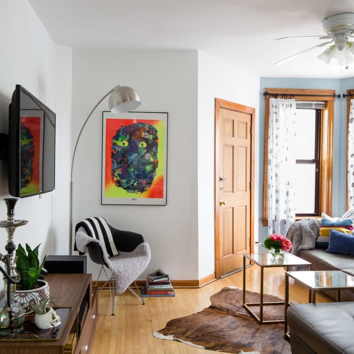Living room with gray sectional sofa, colorful pillows, abstract art, and a cowhide rug. Bright windows with polka dot curtains.