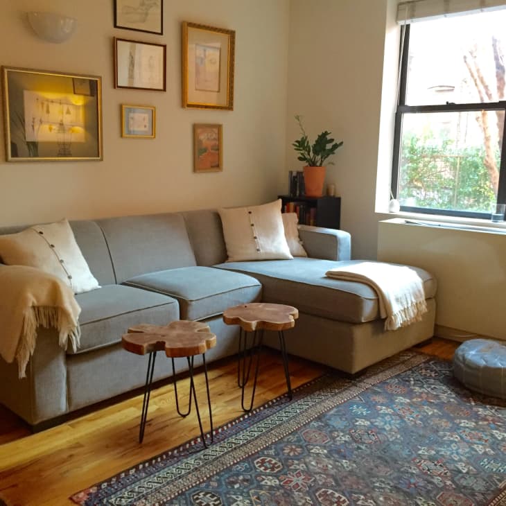 Gray sectional sofa with white pillows and throws, wooden side tables, framed art on walls, and a large window with a view.