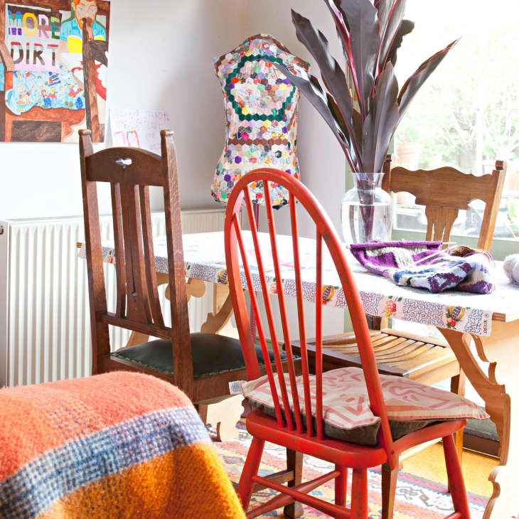 Eclectic dining area with colorful chairs, a patchwork table, vibrant wall art, and a mannequin in a bright room.