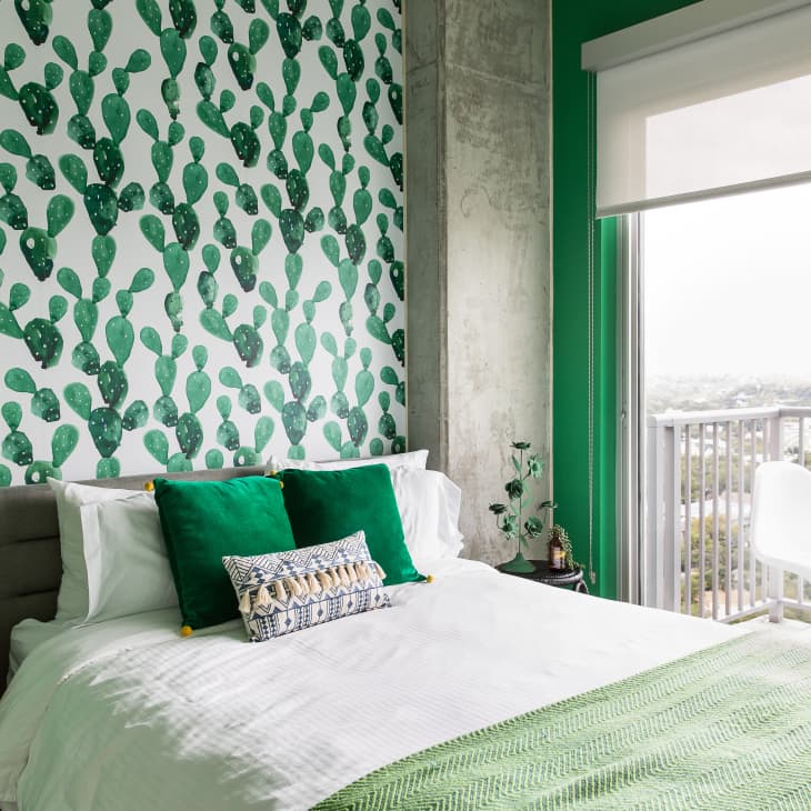 Bedroom with cactus-patterned wallpaper, green accents, white bedding, and a balcony view.