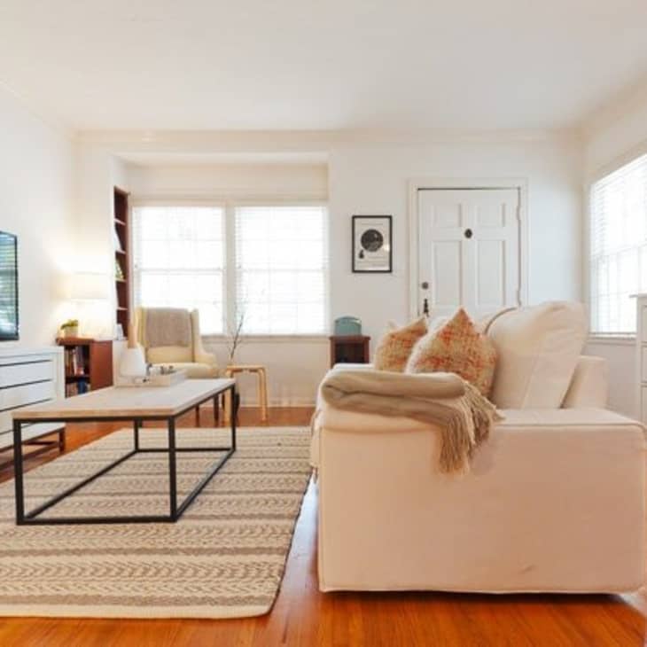 Living room with white sofa, TV on stand, coffee table, and dresser, featuring a patterned rug and framed wall art.