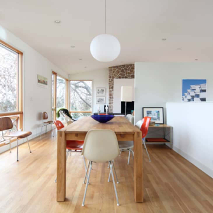 Dining room with wooden table, mixed chairs, large windows, and a blue bowl centerpiece.