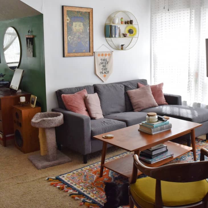 Cozy living room with gray sectional sofa, pink pillows, wooden coffee table, and a cat tree beside a record player.