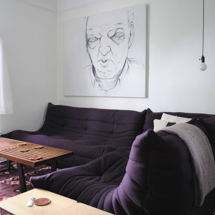 Cozy living room with a dark purple sofa, wooden coffee table, abstract portrait, and bookshelf.