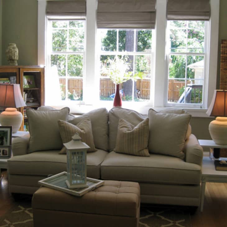 Living room with beige sofa, two side tables with lamps, large windows, and a wooden bookshelf.