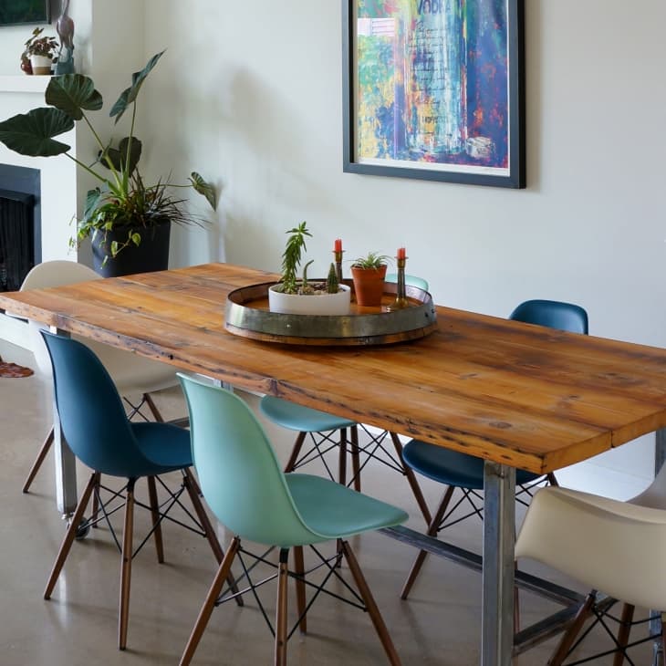 Dining room with a wooden table, mixed color chairs, potted plants, and a fireplace with stacked books.