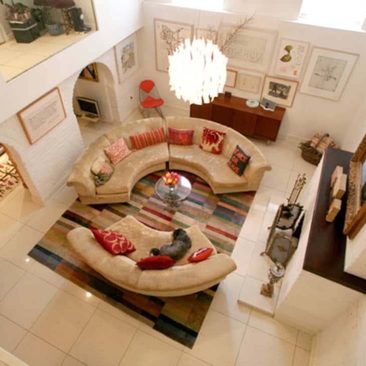 Spacious living room with curved beige sofas, colorful cushions, a striped rug, and a large chandelier.