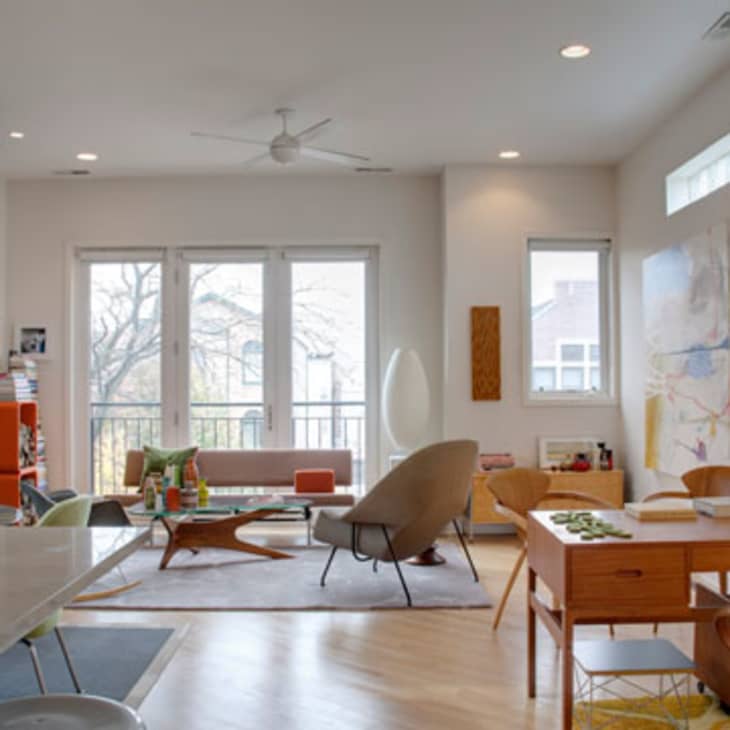 Modern living room with mid-century furniture, large windows, colorful decor, and a dining table with chairs.