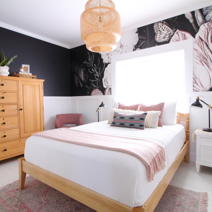 Bedroom with floral wallpaper, wooden bed, pink accents, wicker light fixture, and a wooden dresser.