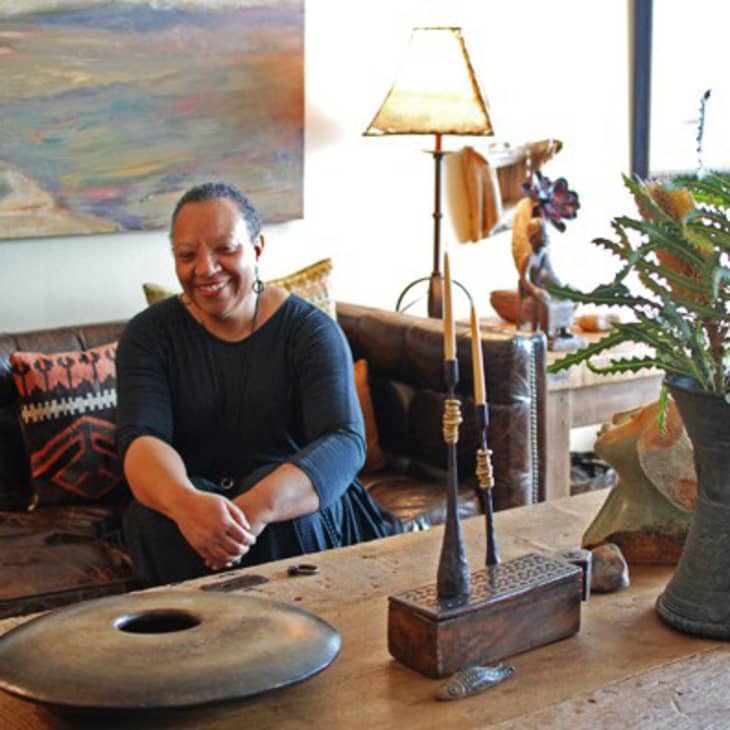 Woman sitting on a leather sofa in a cozy living room with eclectic decor, including a wooden table and vibrant cushions.