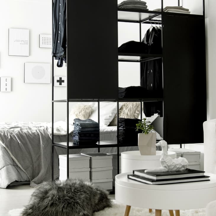 Modern bedroom with black open wardrobe, cozy bed, white round tables, and gray throw blanket on a sofa.
