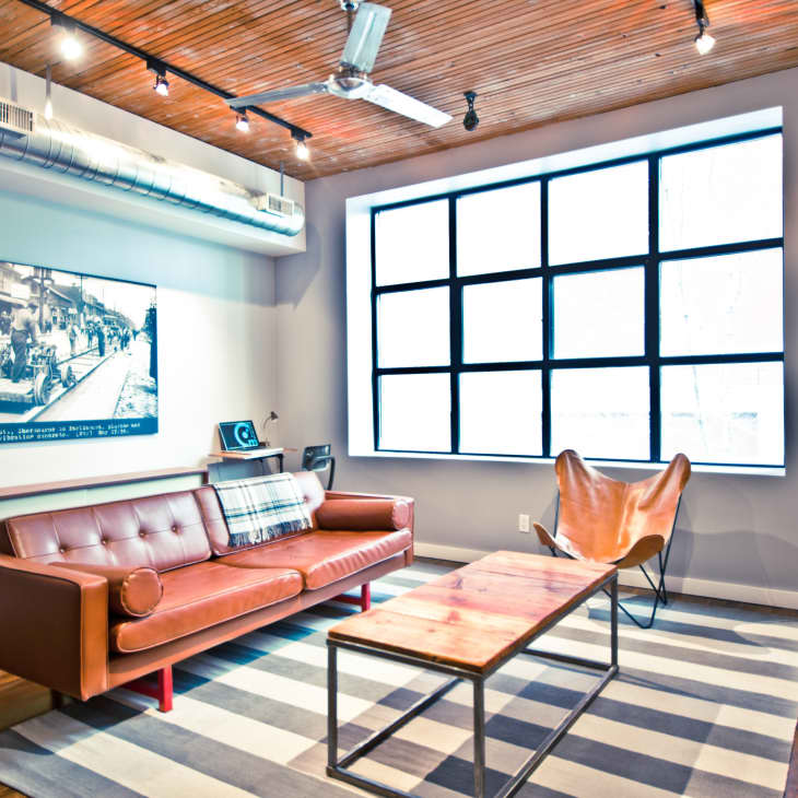 Loft-style living room with brown leather sofa, striped rug, large window, and industrial decor.