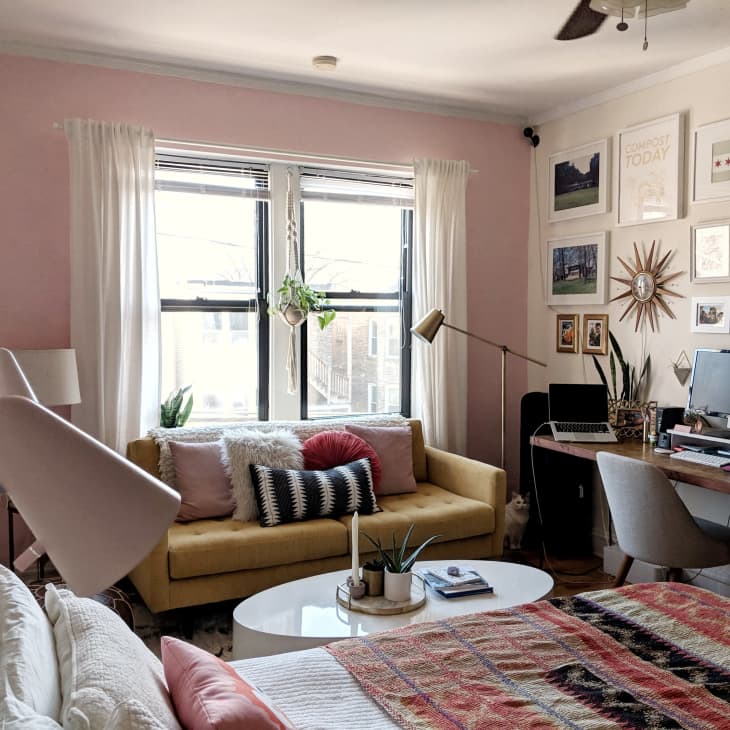 Bedroom with a yellow sofa, pink walls, gallery wall, desk with computer, and a bed with a colorful quilt.