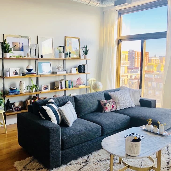 Loft living room with a gray sectional sofa, marble coffee table, and wall shelves filled with books and decor items.