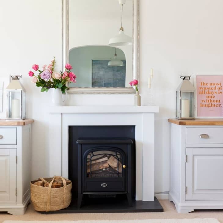 Living room with white fireplace, mirror, pink flowers, lanterns, and framed quote on sideboard.