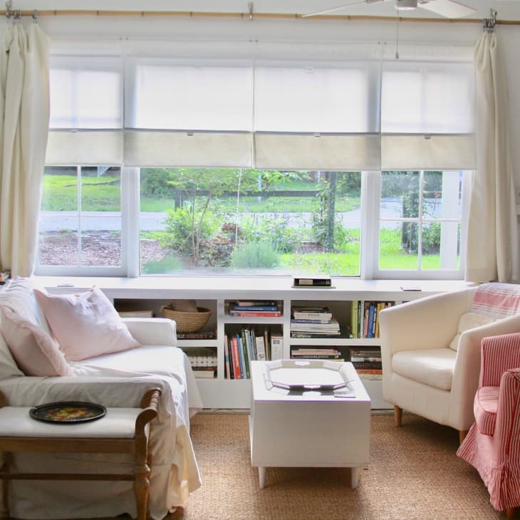 Cozy living room with two armchairs, a white coffee table, bookshelves, and large window with garden view.