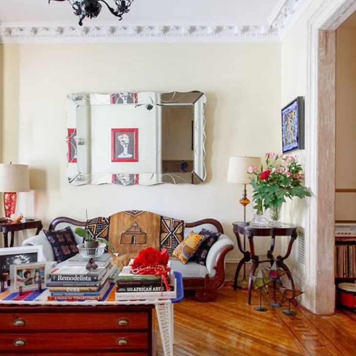 A living room with elaborate crown molding, a large mirror on the wall, and a coffee table covered in books.
