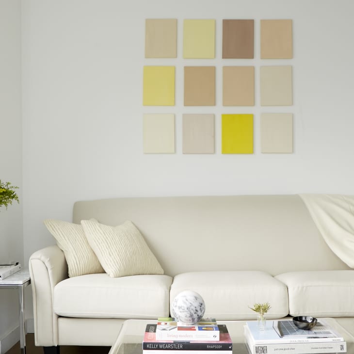 Cream sofa with pillows and throw, abstract wall art, side table with plant, and books on coffee table in a modern living room.