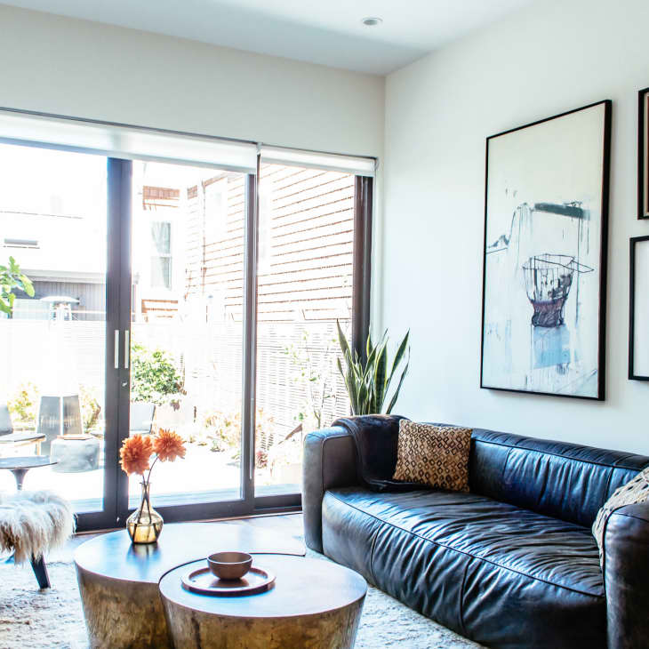 Living room with a black leather sofa, abstract art, fur-covered chair, and sliding glass doors opening to a patio.
