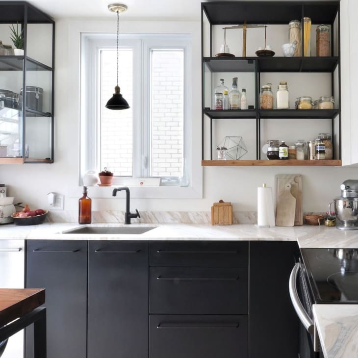 Modern kitchen with black cabinets, open shelves, jars, a mixer, and a pendant light above a marble countertop.
