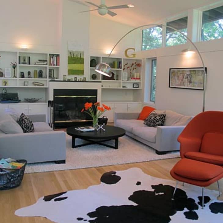 Modern living room with gray sofas, orange chair, black coffee table, cowhide rug, and built-in shelves around a fireplace.