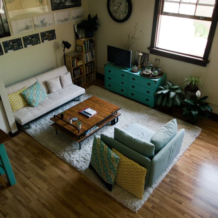 Living room with a white sofa, teal armchair, wooden coffee table, teal dresser, and plants on a light wood floor.