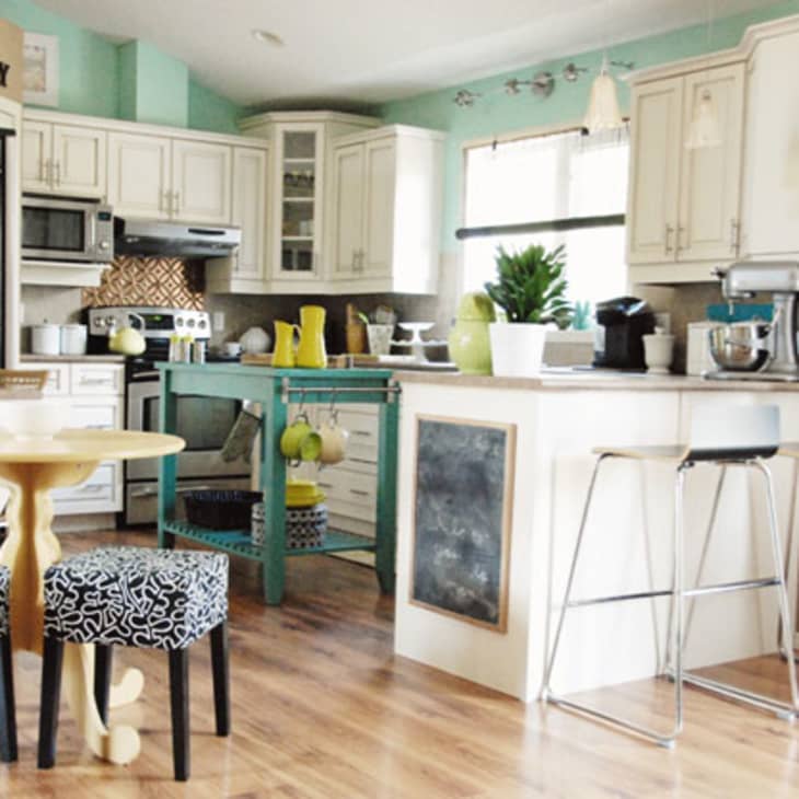 Bright kitchen with white cabinets, teal accents, island, bar stools, and patterned stools around a small round table.