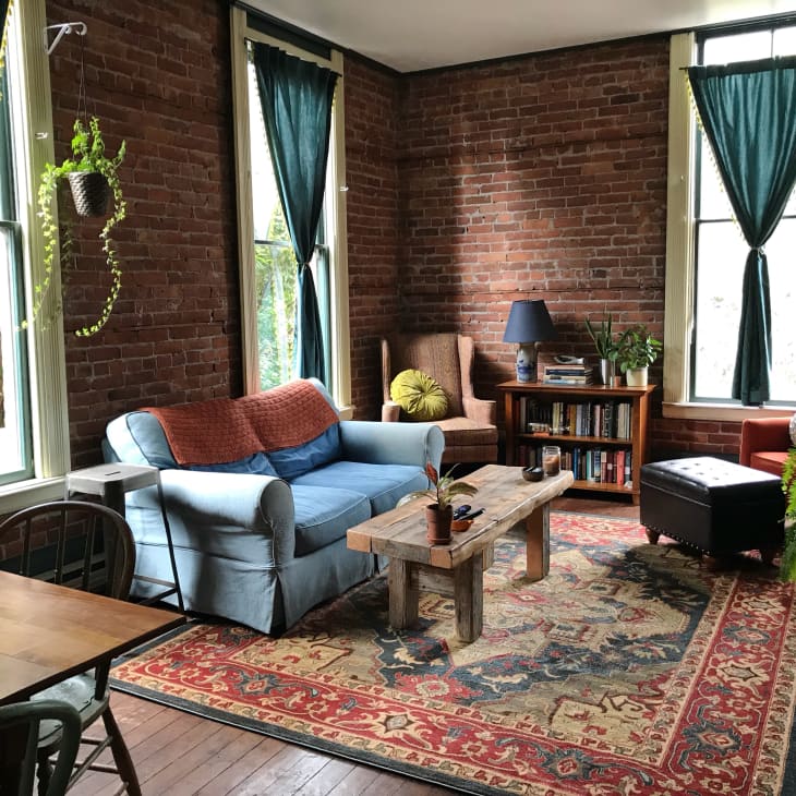 Cozy living room with brick walls, blue sofa, wooden coffee table, bookshelves, and green curtains.