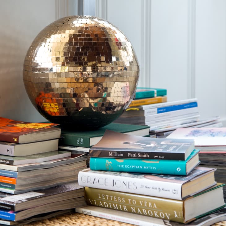 Stack of books topped with a reflective disco ball in a corner of a room.
