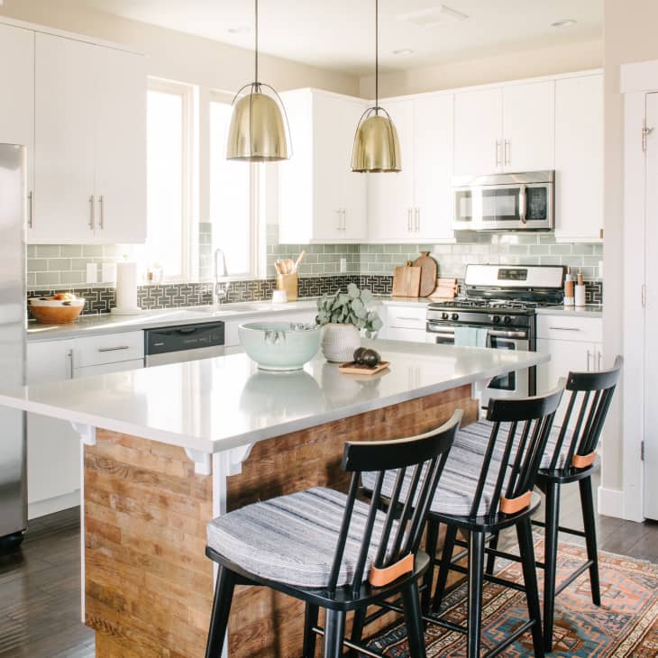 Modern kitchen with white cabinets, stainless steel appliances, island with wooden base, and three black chairs.