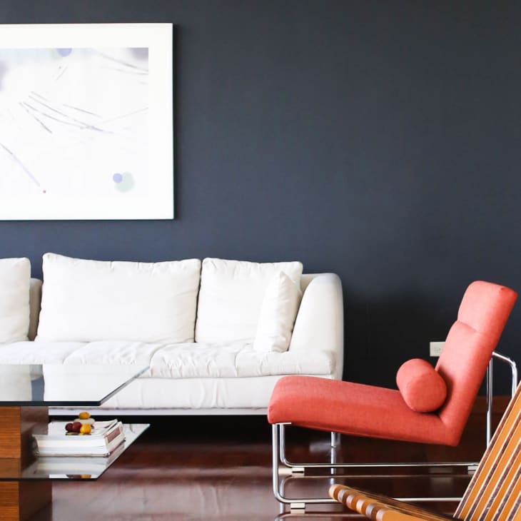Modern living room with white sofa, red lounge chair, glass coffee table, and abstract wall art.