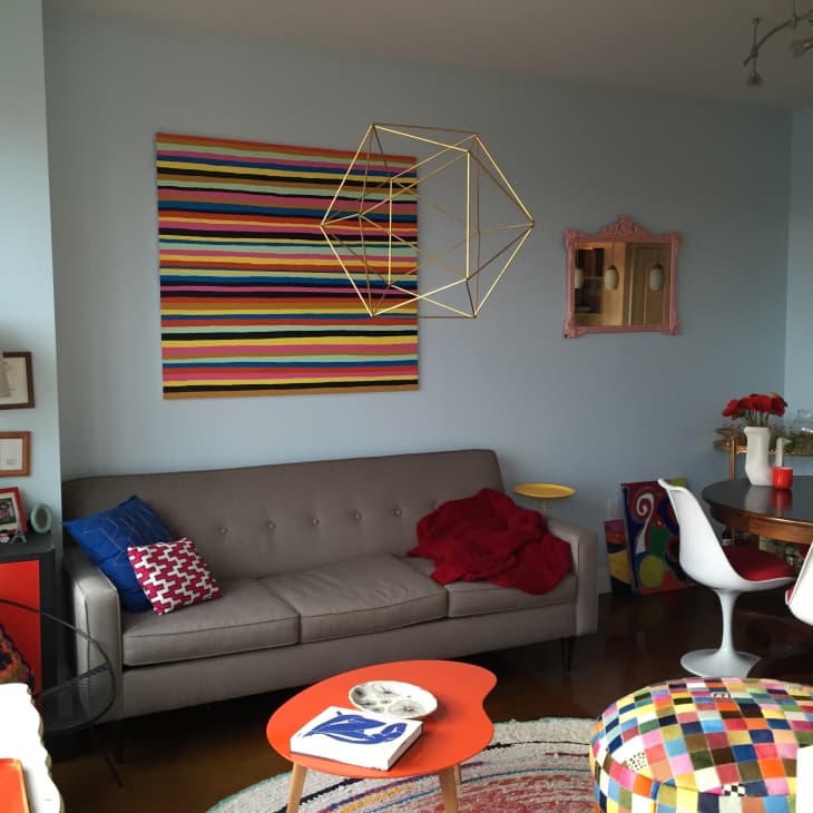 Living room with gray sofa, colorful striped art, geometric sculpture, round dining table, and eclectic decor.