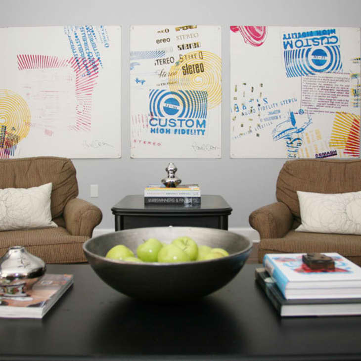 Two brown armchairs with white pillows, abstract art on the wall, and a black table with green apples and books.