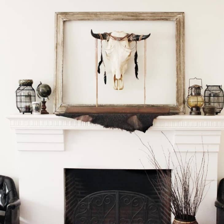 Cow skull decor above a white fireplace with black leather chairs and rustic lanterns.