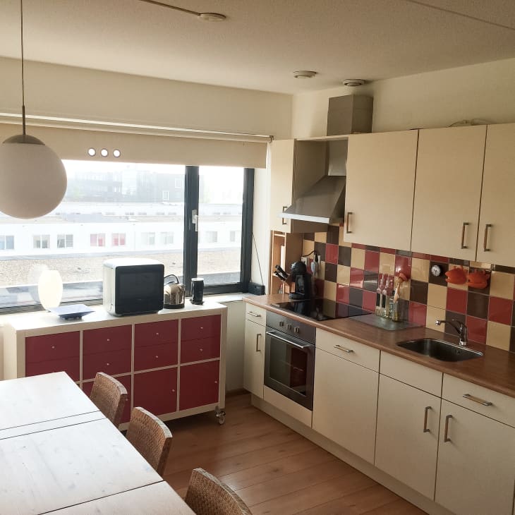 Modern kitchen with white cabinets, red and yellow tiled backsplash, wooden countertops, and a dining table with chairs.