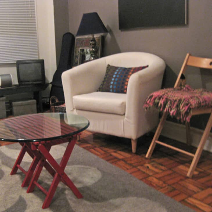 Cozy living room with a white armchair, wooden folding chair, red glass coffee table, and patterned rug.