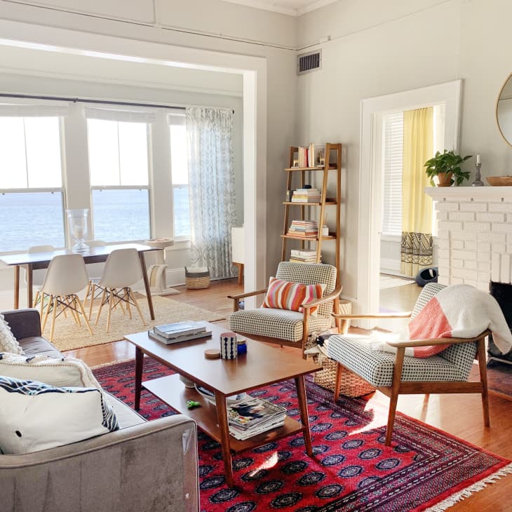Cozy living room with a gray sofa, patterned armchairs, red rug, and a white brick fireplace, overlooking the ocean.