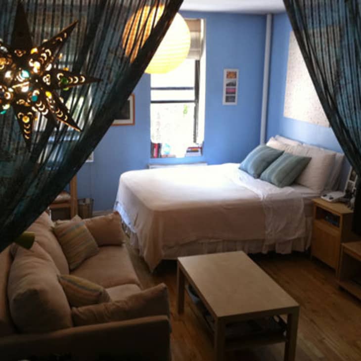 Cozy studio with blue walls, star-shaped light, beige sofa, and bed near window.