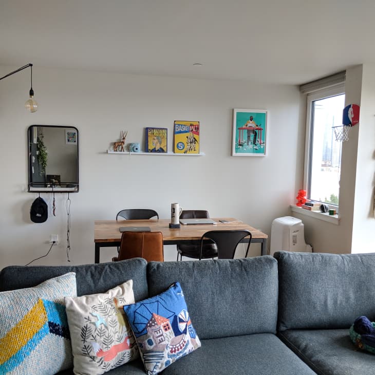Living room with gray sofa, colorful pillows, dining table, wall art, and window with city view.