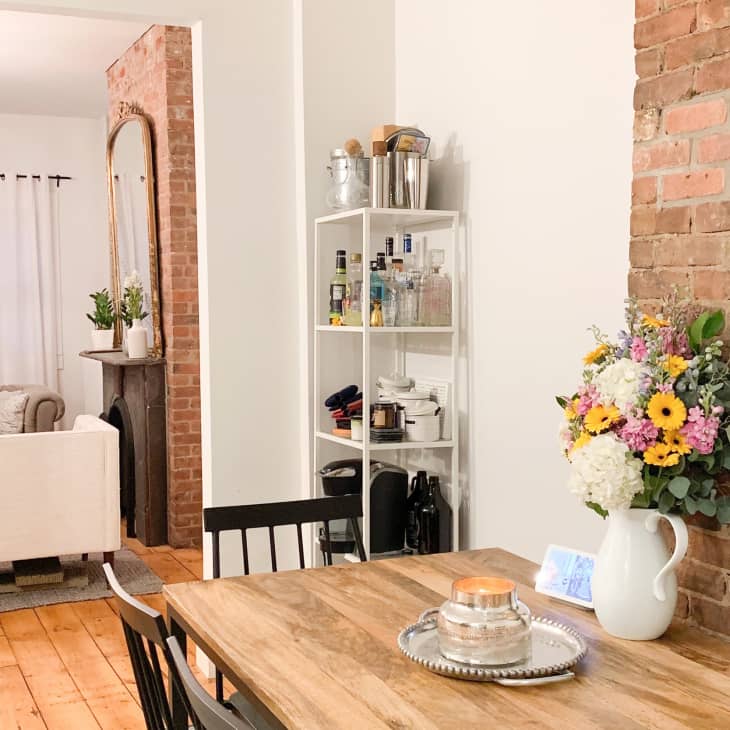 Dining area with wooden table, floral centerpiece, and view into living room with white armchairs and chandelier.