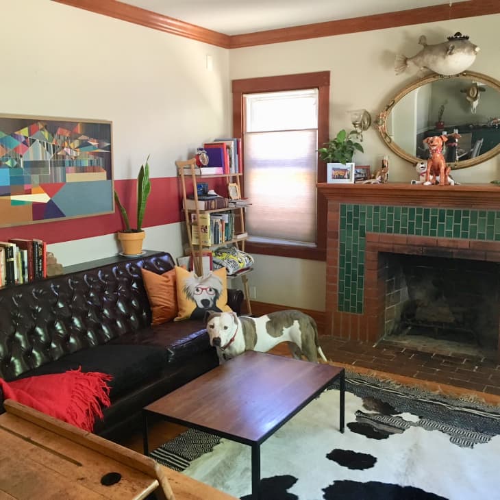 Living room with a dark leather sofa, colorful abstract art, green-tiled fireplace, and a dog on a cowhide rug.