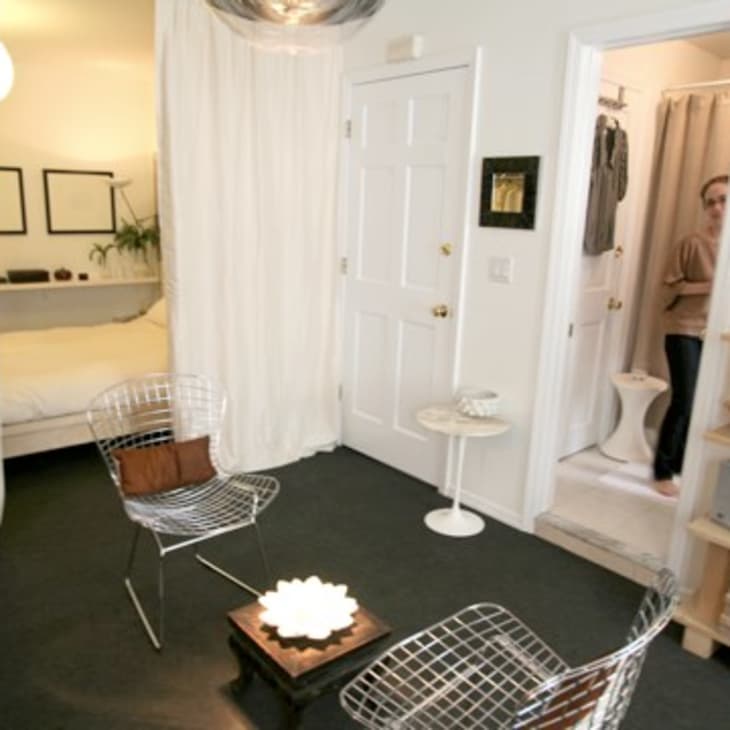 Small living room with wire chairs, a low table, and a view into a bedroom and bathroom.