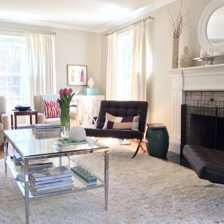 Bright living room with white rug, glass coffee table, black chairs, and a fireplace. Pink tulips on the table.