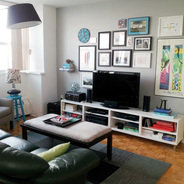 Living room with a black leather sofa, TV, gallery wall, and colorful decor on a white media console.