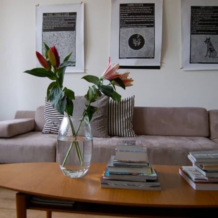Living room with a beige sofa, floral vase on a wooden table, and three framed artworks on the wall.