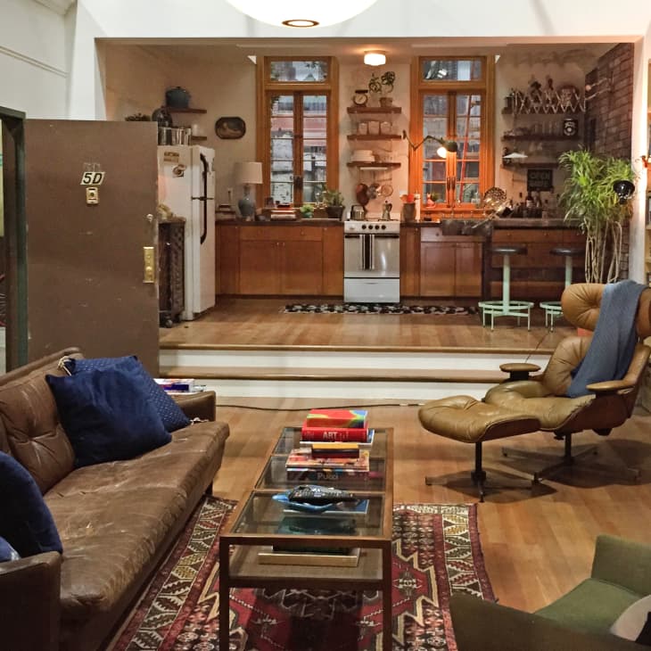 Cozy living room with brown leather sofa, blue cushions, vintage armchair, globe, and open kitchen with wooden cabinets.