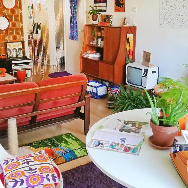 Retro living room with vintage TVs, orange sofa, typewriter, plants, and colorful decor.